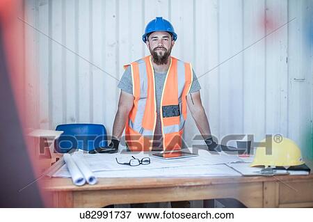 Portrait of young male construction worker standing at desk in portable cabin View Large Photo Image Stock Photo - Portrait of young male construction worker standing at desk in portable cabin. Fotosearch