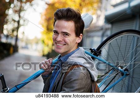 Portrait of young man carrying cycle on shoulders along sidewalk View Large Photo Image Stock Photo - Portrait of young man carrying cycle on shoulders along sidewalk. Fotosearch