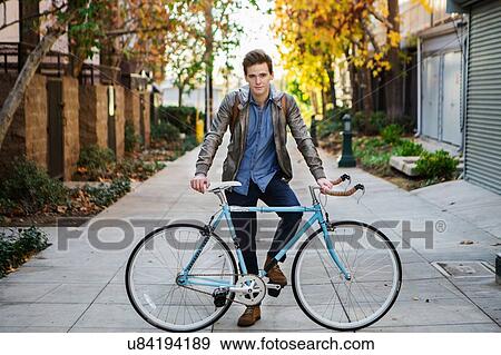 Stock Photo - Portrait of young man leaning against cycle on sidewalk. Fotosearch
