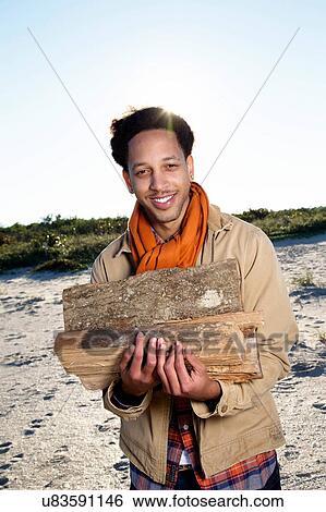 "Portrait of young man on beach, holding fire wood, smiling" View Large Photo Image Stock Photograph - "Portrait of young man on beach, holding fire wood, smiling". Fotosearch