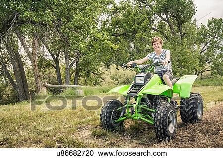 Stock Image - Portrait of young man riding quad bike in field. Fotosearch
