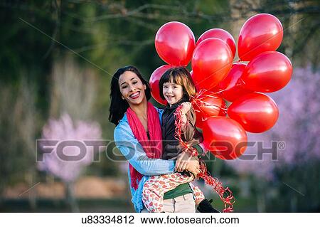 Portrait of young woman and daughter with bunch of red balloons in park View Large Photo Image Stock Image - Portrait of young woman and daughter with bunch of red balloons in park. Fotosearch