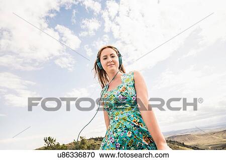 Stock Image - Portrait of young woman listening to headphones in hilly landscape, Bridger, Montana, USA. Fotosearch