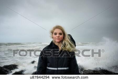 Picture - Portrait of young woman with smudged mascara standing in front of splashing ocean waves. Fotosearch