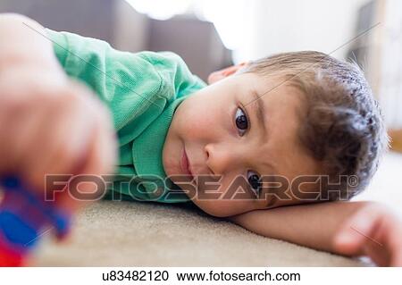 "Preschool boy lying on carpet playing with toy, looking away" View Large Photo Image Stock Image - "Preschool boy lying on carpet playing with toy, looking away". Fotosearch