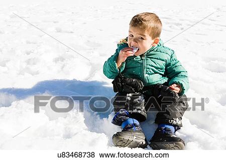 Stock Photo - Preschool boy sitting on snow covered ground eating snow. Fotosearch
