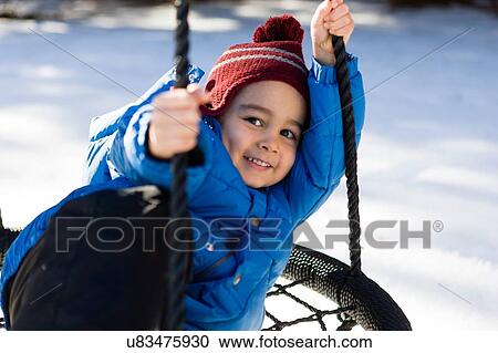 Stock Image - "Preschool boy wearing knit hat on hammock swing, looking at camera smiling". Fotosearch