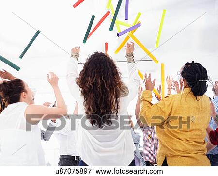 Stock Photo - Rear view of colleagues in team building task throwing colourful tubes in the air. Fotosearch