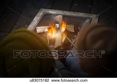 Rear view of couple wearing knit hats toasting marshmallows on camp fire at night View Large Photo Image Stock Image - Rear view of couple wearing knit hats toasting marshmallows on camp fire at night. Fotosearch