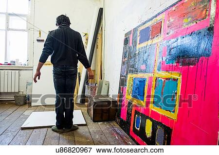 Stock Photo - Rear view of male artist standing in front of blank canvas. Fotosearch