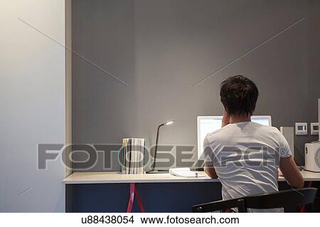 Picture - Rear view of man sitting at desk using desktop computer. Fotosearch
