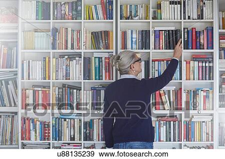 Rear view of mature woman selecting book from bookshelves View Large Photo Image Stock Photo - Rear view of mature woman selecting book from bookshelves. Fotosearch