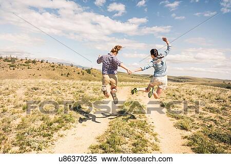 Rear view of two young women jumping mid air over dirt track, Bridger, Montana, USA View Large Photo Image Stock Photography - Rear view of two young women jumping mid air over dirt track, Bridger, Montana, USA. Fotosearch