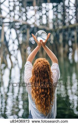 Rear view of woman holding up crystal ball in front of wood river pier View Large Photo Image Stock Image - Rear view of woman holding up crystal ball in front of wood river pier. Fotosearch