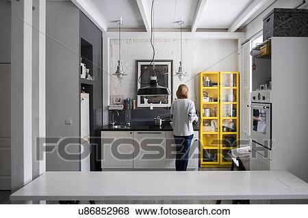 Stock Photo - Rear view of woman preparing food at kitchen hob. Fotosearch