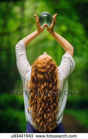 Rear view of young woman with long red hair holding up crystal ball in forest View Large Photo Image Stock Image - Rear view of young woman with long red hair holding up crystal ball in forest. Fotosearch