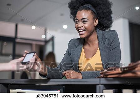 Stock Image - Receptionist handing young businesswomen smartphone at office reception. Fotosearch