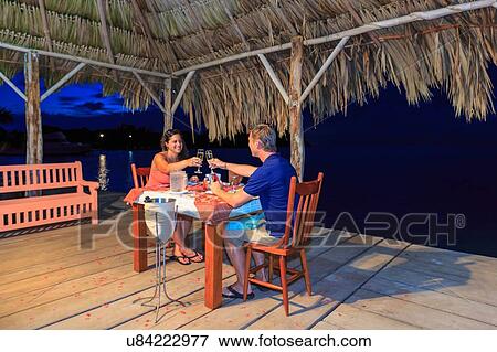 Stock Photo - "Romantic couple raising a champagne toast at waterfront restaurant, St. Georges Caye, Belize, Central America". Fotosearch