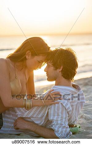 Stock Photograph - Romantic young couple reclining on beach at sunset, Majorca, Spain. Fotosearch