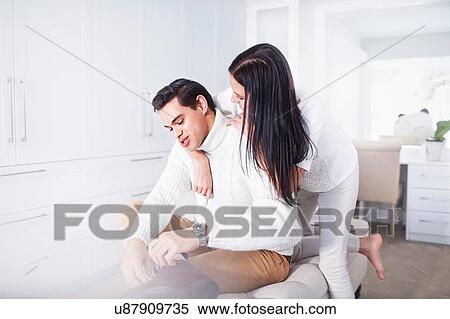 Stock Photography - Romantic young couple sitting on ottoman in bedroom. Fotosearch