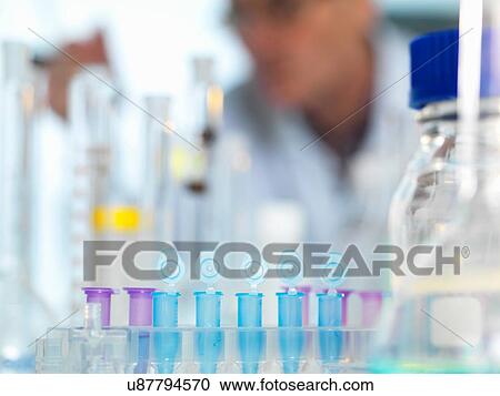 Stock Image - Row of eppendorf vial awaiting sample for testing in laboratory, scientist out of focus in background. Fotosearch
