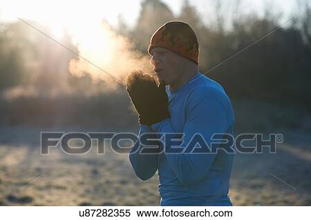 Stock Photography - Runner wearing knit hat and gloves, rubbing hands together, breathing cold air. Fotosearch