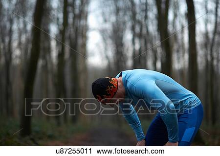 Stock Image - Runner wearing knit hat and spandex bending forward hands on knees exhausted. Fotosearch
