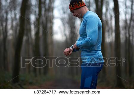 Stock Photo - Runner wearing knit hat and spandex looking down at wrist watch. Fotosearch
