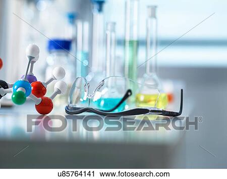 Stock Image - Safety glasses and molecular model on laboratory bench, scientific equipment in background. Fotosearch