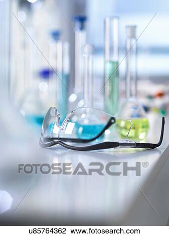 Stock Image - Safety glasses on laboratory bench, scientific equipment in background. Fotosearch