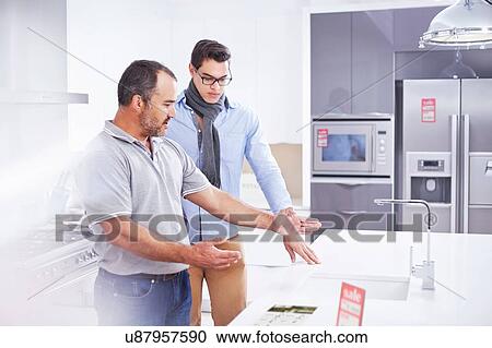 Stock Image - Salesman and young man in kitchen showroom. Fotosearch