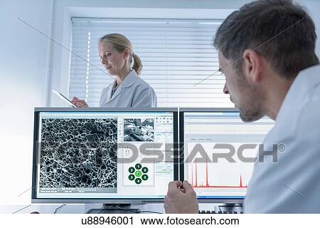 Stock Image - Scientists with electron microscope screens. Fotosearch