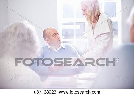 Stock Image - Secretary handing paperwork to businessman in office. Fotosearch