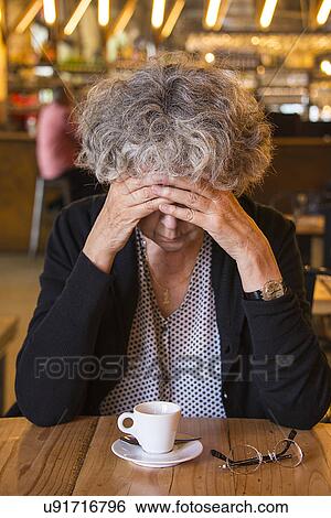 Stock Photograph - Senior woman in cafe with head in hands. Fotosearch