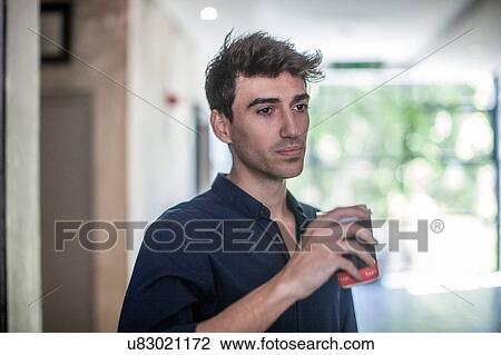 Stock Image - Serious young businessman drinking takeaway coffee in office. Fotosearch