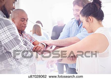 Stock Image - Side view of colleagues in team building task holding wrists smiling. Fotosearch