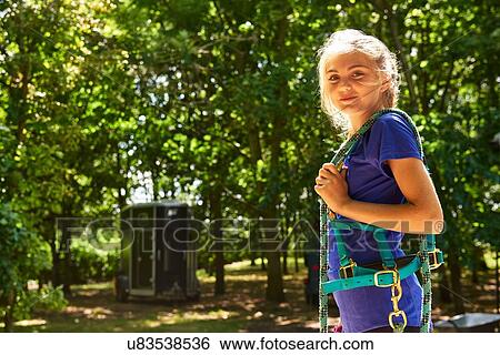 Stock Photograph - Side view of girl carrying horse reins over shoulder looking at camera smiling. Fotosearch