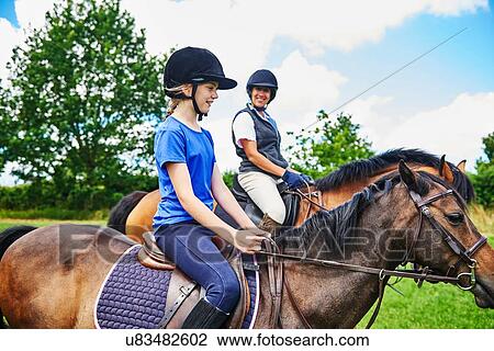 Side view of mature woman and girl on horseback wearing riding hats smiling View Large Photo Image Stock Image - Side view of mature woman and girl on horseback wearing riding hats smiling. Fotosearch