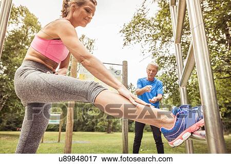 Stock Photo - Side view of mature woman leg raised on playground equipment bending forward stretching. Fotosearch