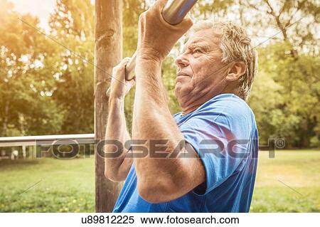 Stock Photography - Side view of senior man in park doing pull up on metal bar. Fotosearch