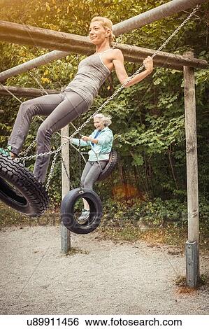 Stock Photograph - Side view of women standing on tyre swings, swinging. Fotosearch