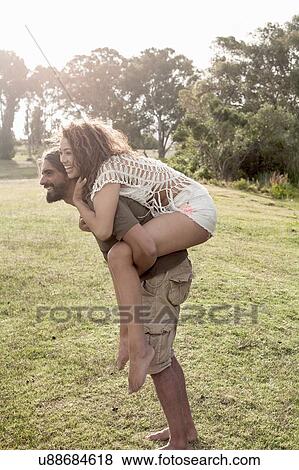 Side view of young man bending forward giving young woman piggyback smiling View Large Photo Image Stock Photo - Side view of young man bending forward giving young woman piggyback smiling. Fotosearch