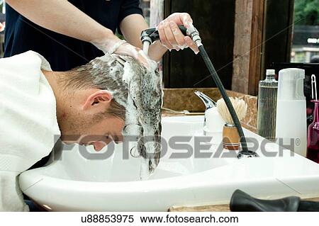 Stock Photography - Side view of young man bending forward having hair washed in barbershop. Fotosearch