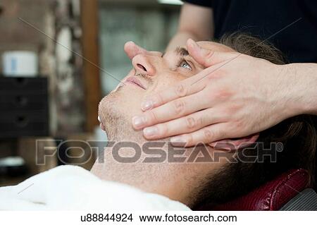 Picture - Side view of young mans head and shoulders having facial massage. Fotosearch
