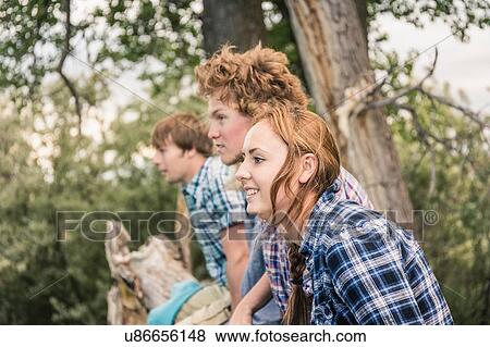 Side view of young men with woman sitting together on fallen tree View Large Photo Image Stock Photo - Side view of young men with woman sitting together on fallen tree. Fotosearch