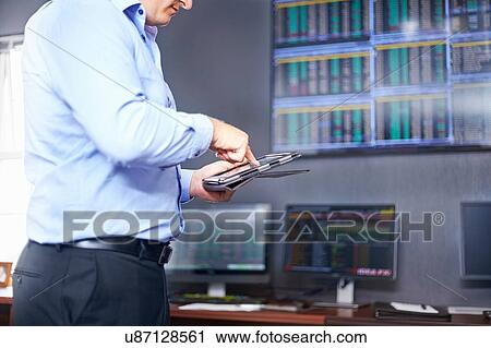 Stock Image - Side view of young mid adult mans mid section in office using digital tablet. Fotosearch