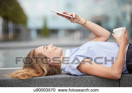 Side view of young woman lying on back on wall using smartphone smiling View Large Photo Image Stock Image - Side view of young woman lying on back on wall using smartphone smiling. Fotosearch