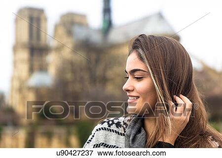 Stock Photo - Side view of young woman, Notre Dame Cathedral in background, Paris, France. Fotosearch