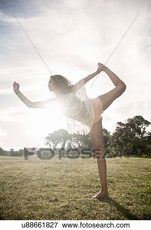 Stock Photo - Side view of young woman standing on one leg holding foot looking away. Fotosearch