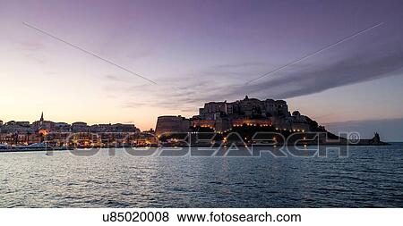 Stock Photo - Silhouetted view of sea and Calvi at dusk, Corsica, France. Fotosearch